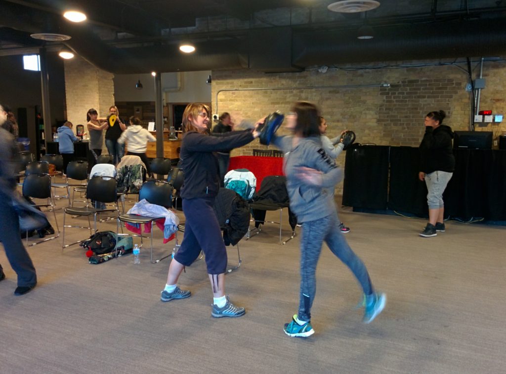 Participants practising pad strikes with partners during a group self-defense seminar