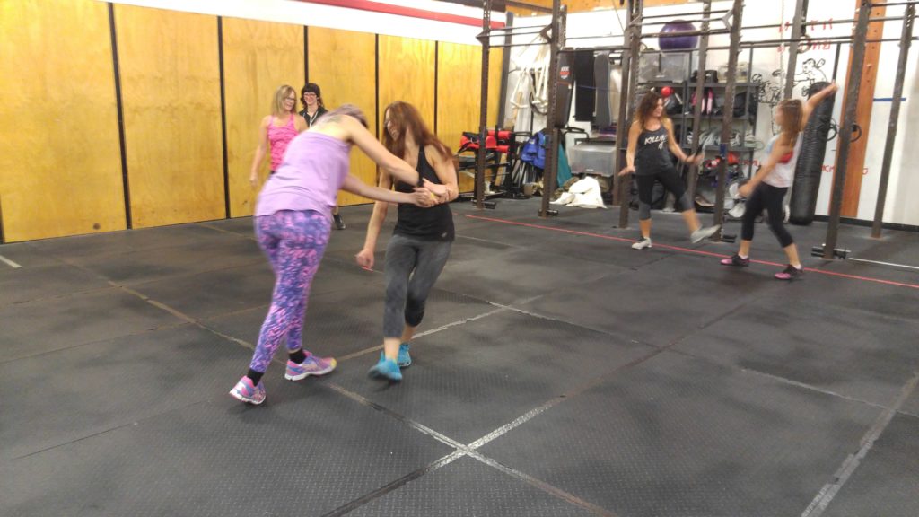Participants practising partner self-defense drills on gym mats